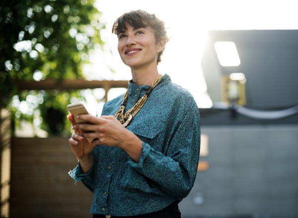 ▲“A smiling woman in an azure blouse holding a smartphone while standing outdoors”。（圖／rawpixel on Unsplash）